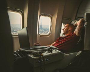 Comfortable flights to South Africa: Man relaxing on a plane with a laptop, Eiffel Tower view.